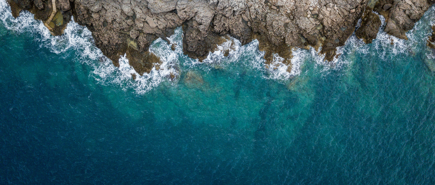 overhead image of waves crashing against jagged rocks