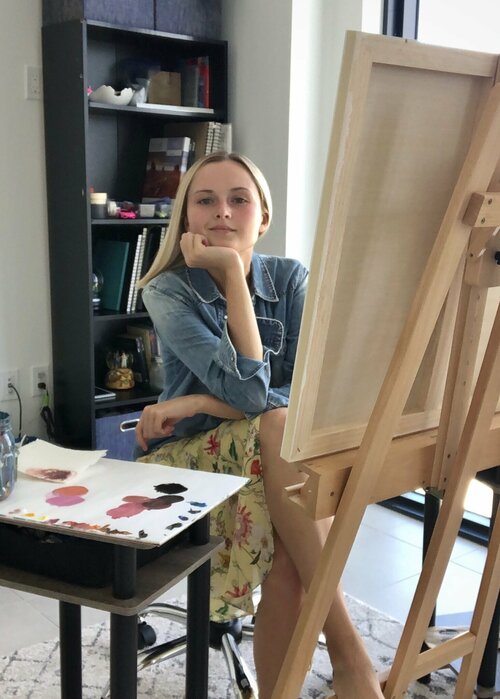artist Irina Pushkareva sitting in front of easel with head propped on hand