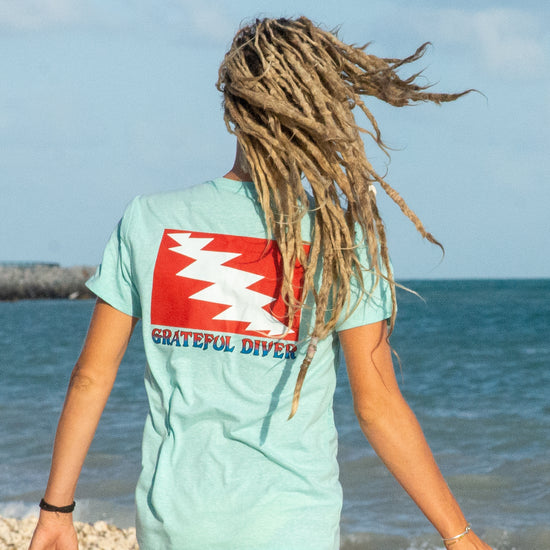 back of woman wearing a mint Grateful Diver Classic T-shirt in front of ocean