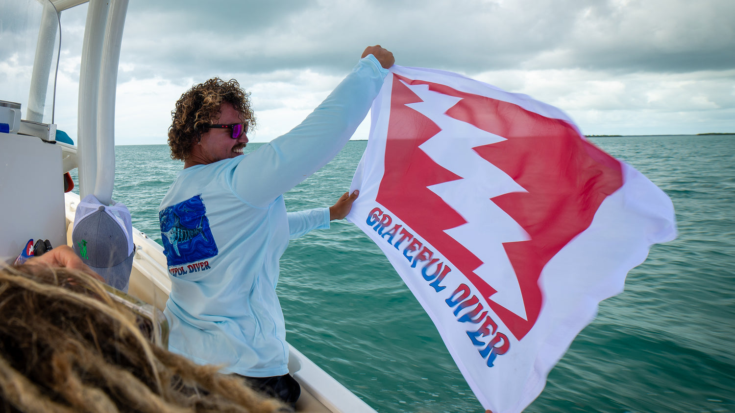 man holding Grateful Diver classic lightning bolt dive flag on a boat while cruising through the ocean