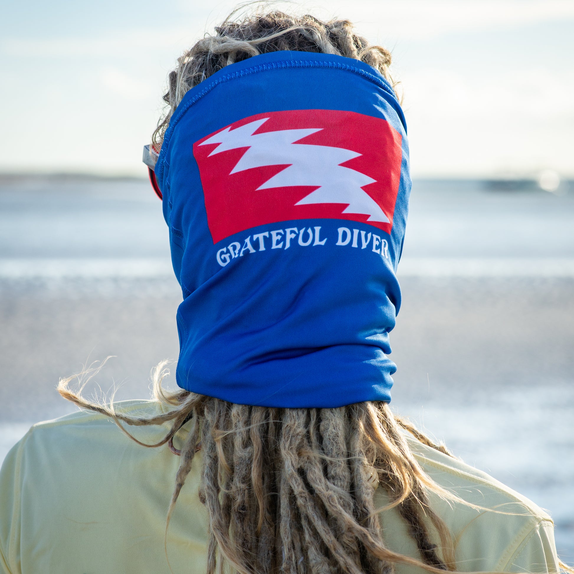 Grateful Diver Classic Dive Flag Neck Gaiter worn as a mask showing lightning bolt logo on back of model's head in front of ocean