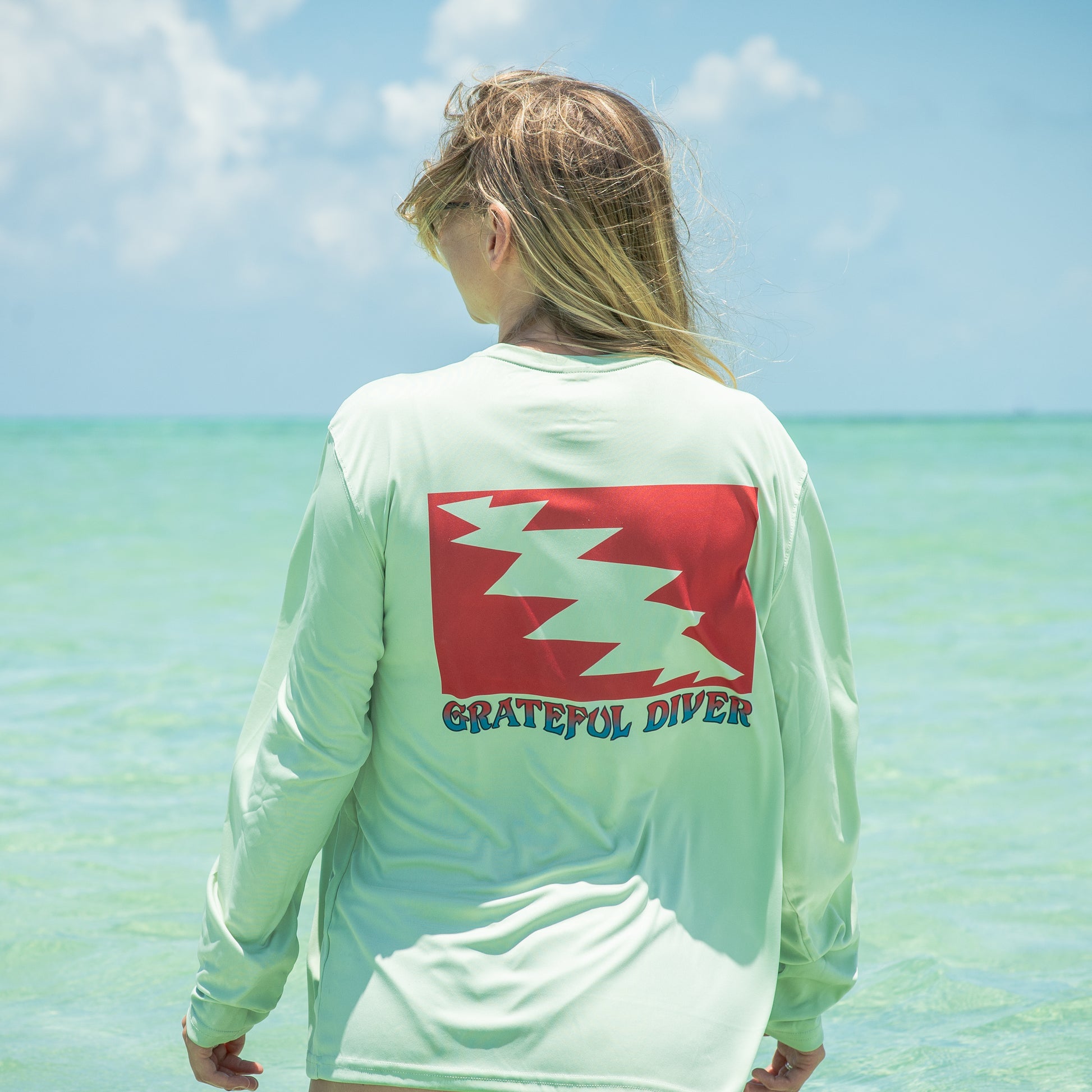 Grateful Diver Classic UV Shirt in sage back shot on woman in front of ocean