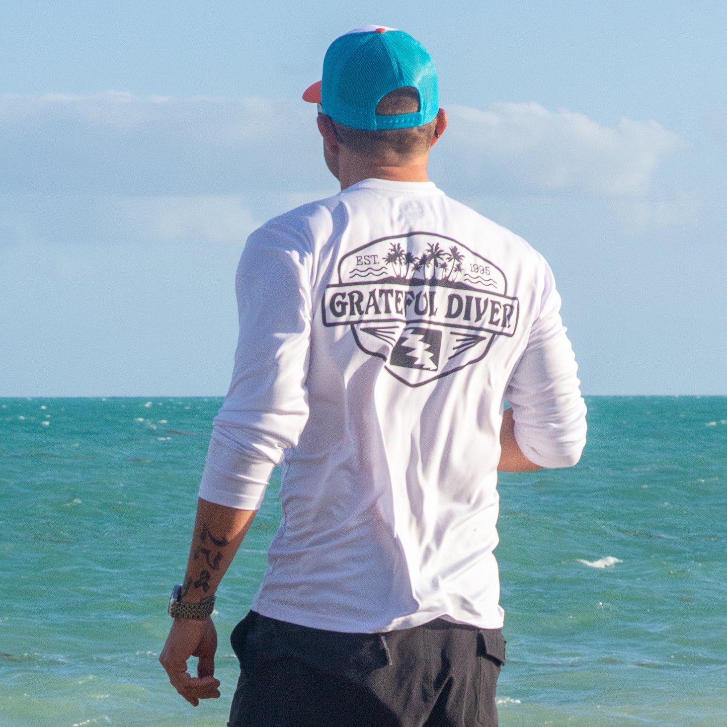 Grateful Diver Palm Tree UV Shirt in white showing the back on model in front of ocean