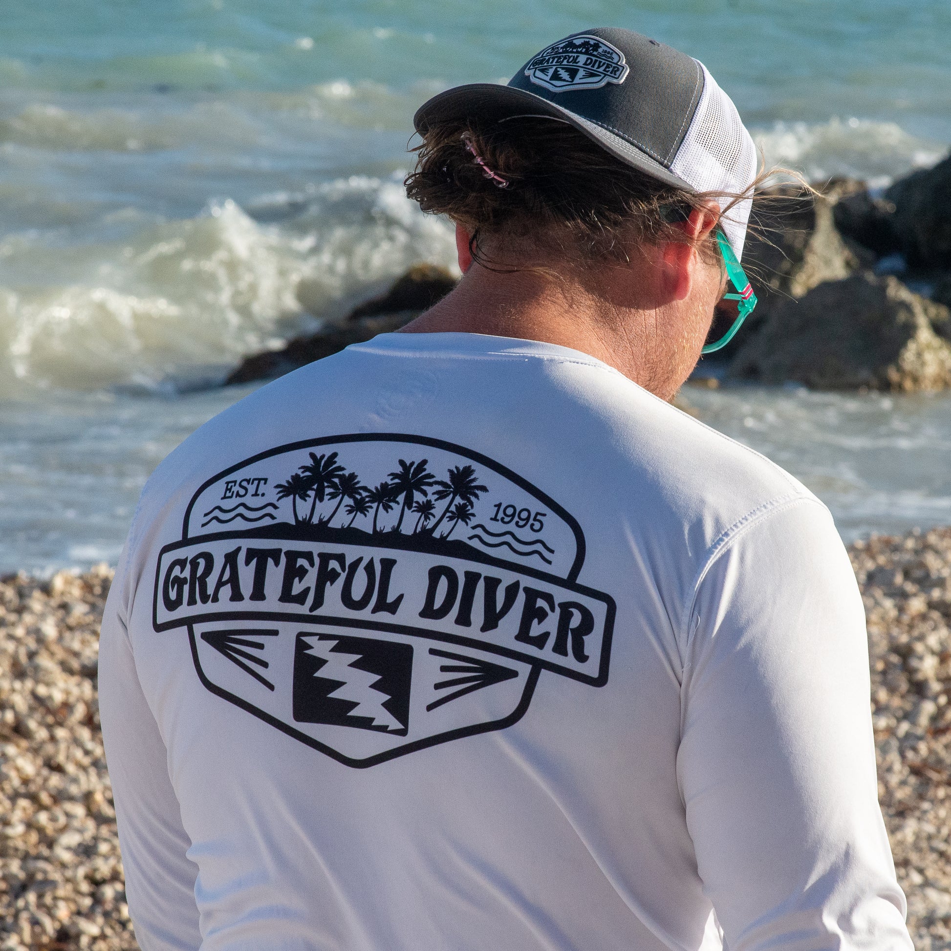 Grateful Diver Palm Tree UV Shirt in white showing the back back on model on ocean rocks