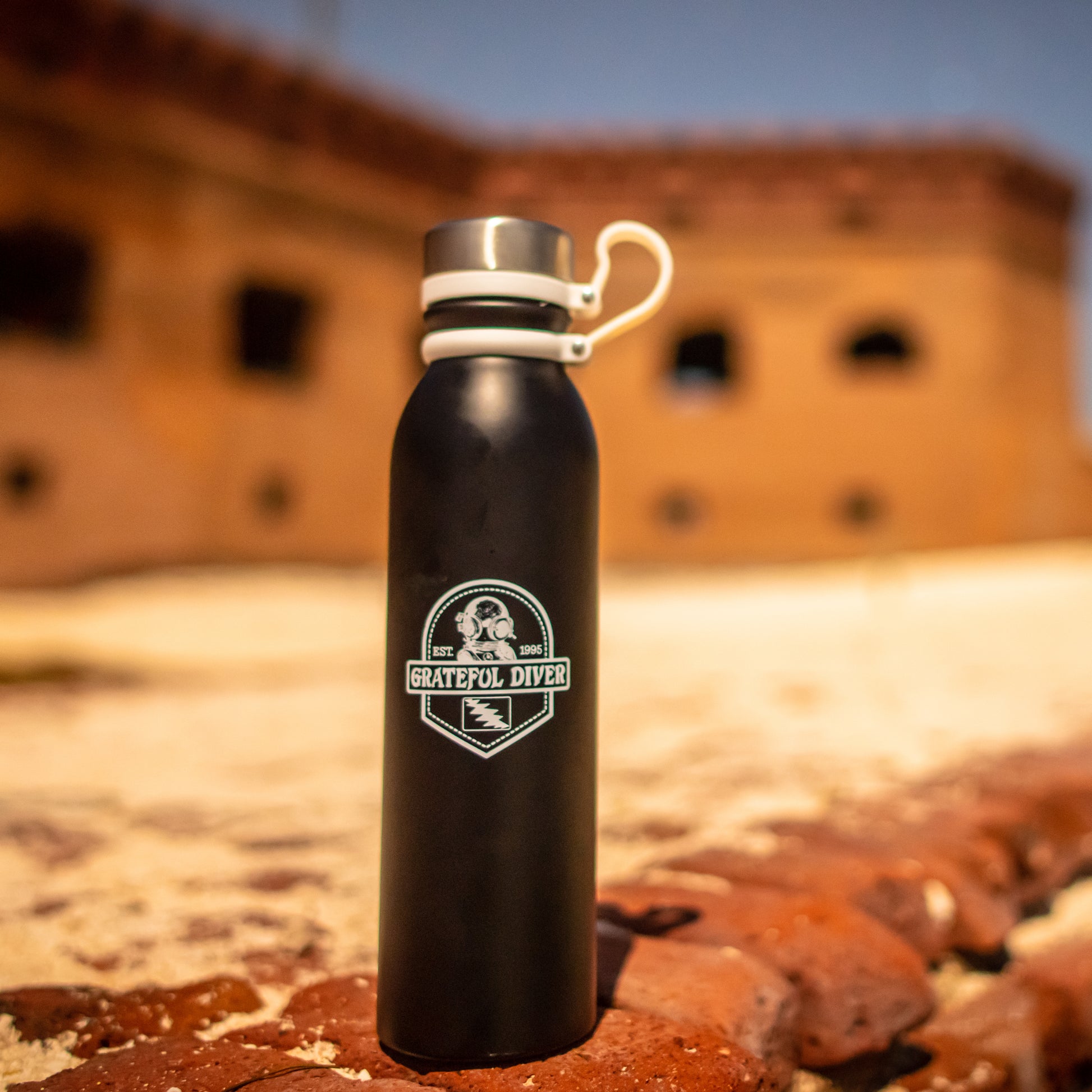 Grateful Diver Dive Helmet 25-oz. Stainless Steel Water Bottle on red clay rocks in front of adobe building